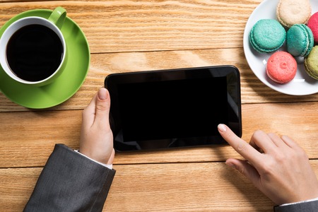 Top view of female hands using tablet device while sitting at wooden tableの写真素材