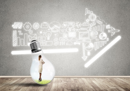 Businesswoman inside of light bulb in empty concrete roomの写真素材