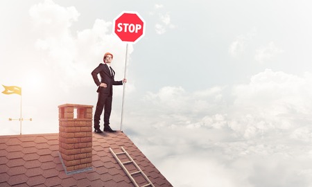 Caucasian businessman on brick house roof showing stop road signの写真素材