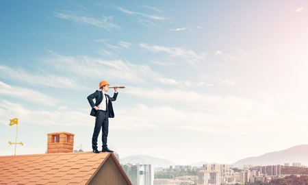 Engineer man standing on roof and looking in spyglass. Mixed medの写真素材