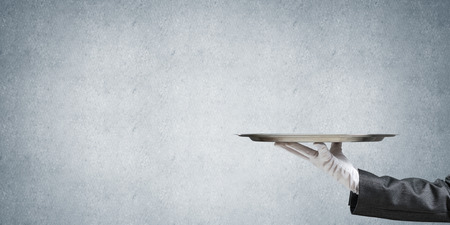 Hand of butler holding empty metal tray against concrete backgroundの写真素材