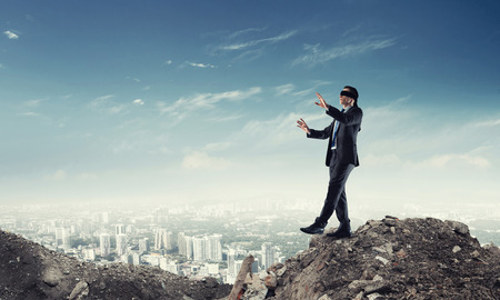 Young businessman in blindfold walking carefully and cityscape at backgroundの写真素材