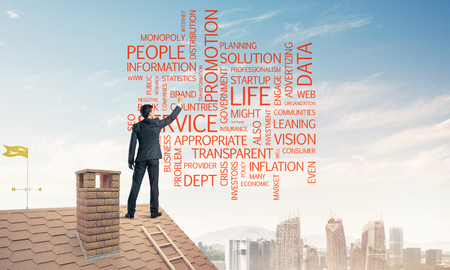 Young businessman standing on house roof and writing leadershipの写真素材
