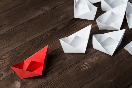 Business leadership concept with white and color paper boats on wooden tableの写真素材