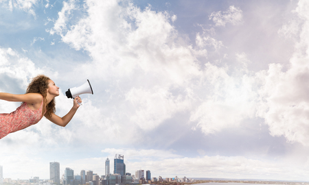 Young woman in dress making announcement in megaphoneの写真素材