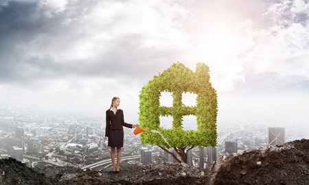 Young attractive businesswoman watering plant in ground with can against the backdrop of the cityの写真素材