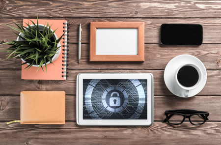Business workplace with office stuff and tablet with padlock icons on screenの写真素材