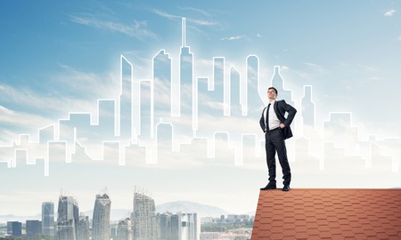 Young determined businessman standing on house roof and looking away. Mixed mediaの写真素材