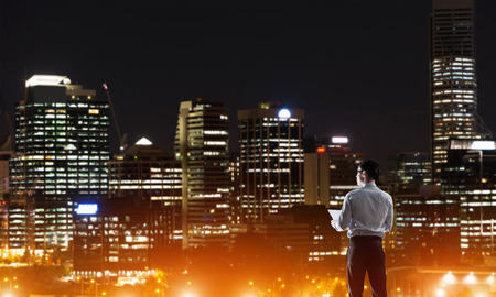 Elegant businessman with suitcase looking at night cityの写真素材