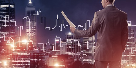 Rear view of businessman against modern cityscape holding papers in handの写真素材