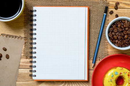 Opened notepad and cup of coffee with donut on wooden table