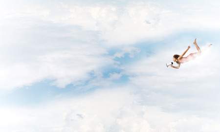 Young woman with megaphone flying high in skyの写真素材