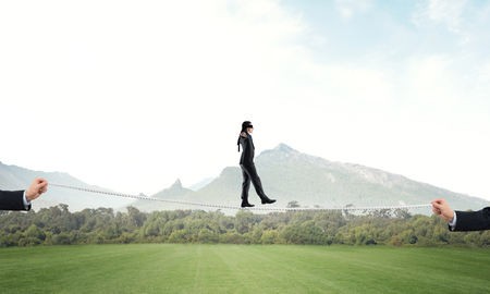 Businessman with blindfolder on eyes walking on rope over natural backgroundの写真素材