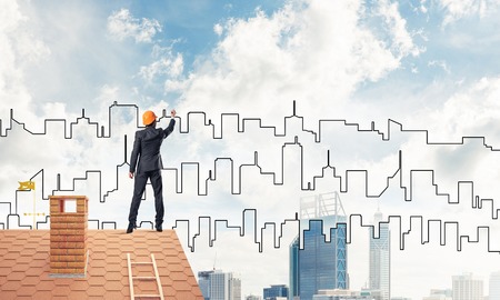 Engineer man standing with back on house roof and drawing city. Mixed mediaの写真素材