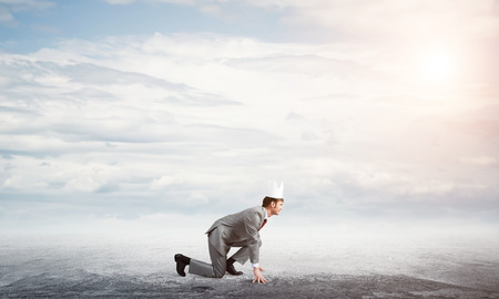 Young handsome businessman wearing white paper crown running in a hurryの写真素材