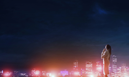 Rear view of elegant businesswoman talking mobile and viewing lights of night cityの写真素材