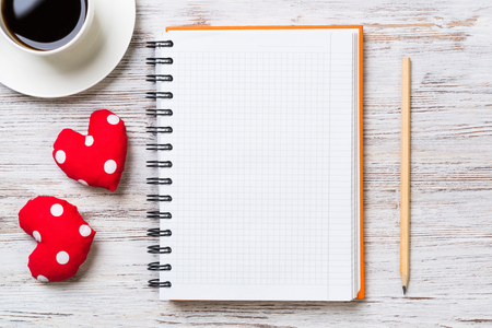 Coffee cup notepad pencil and two red hearts on wooden surfaceの写真素材