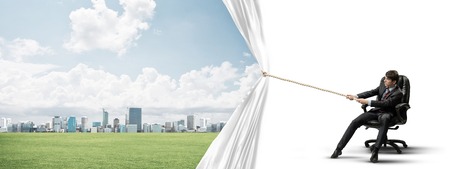 Businessman sitting in chair and pulling white blank fabric. Place for textの写真素材