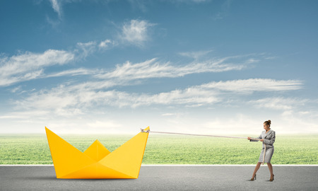 Successful businesswoman pulling with rope paper boatの写真素材