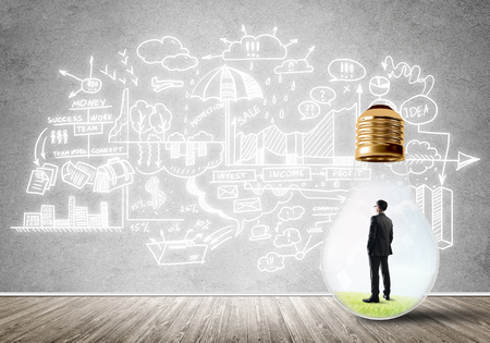 Businessman inside of light bulb in empty concrete room and sketches on wallの写真素材