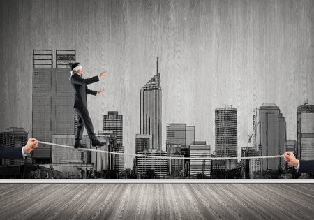 Businessman with blindfolder on eyes walking on ropeの写真素材