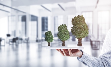 Close of businessman holding tablet pc with green tree made of gears and cogwheels. Mixed mediaの写真素材