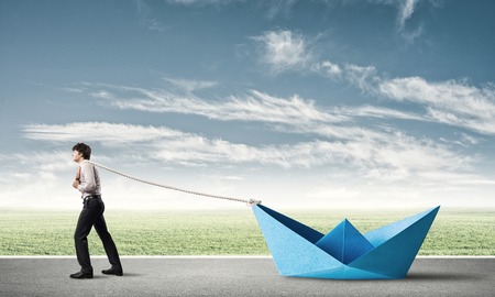 Successful businessman pulling with rope paper boatの写真素材