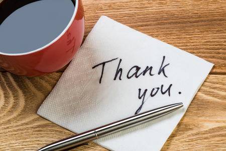 Coffee cup pen and napkin with words on wooden tableの写真素材