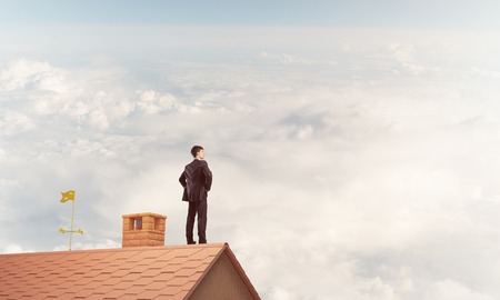 Young determined businessman standing with back on house roof and looking away. Mixed mediaの写真素材