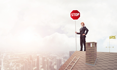 Businessman standing on house roof and holding stop sign. Mixed mediaの写真素材