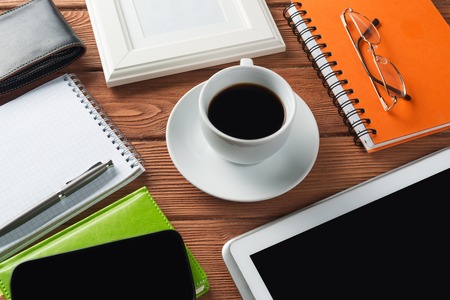 Still life photo of tablet notepad coffee glasses and other stuff on wooden tableの写真素材