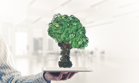 Close of businessman holding tablet pc with green tree made of gears and cogwheels. Mixed mediaの写真素材