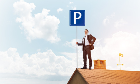 Businessman on house top holding car parking board and viewing city. Mixed mediaの写真素材