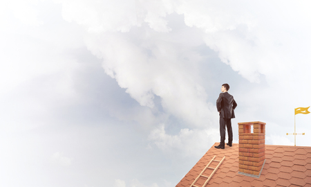 Young determined businessman standing with back on house roof and looking away. Mixed mediaの写真素材