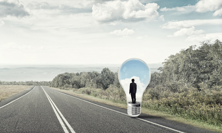 Young businessman trapped inside of light bulb on asphalt roadの写真素材