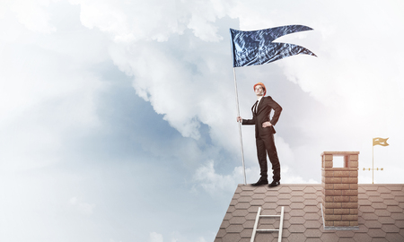 Businessman standing on house roof and holding blue flag. Mixed mediaの写真素材