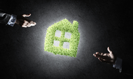 Close of businessman hand and green house icon as symbol of save constructionの写真素材