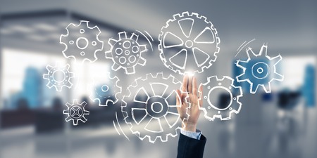 Close of businesswoman hand touching gears on screen with palm and office at backgroundの写真素材