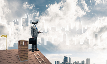 Faceless businessman with camera zoom instead of head standing on house roofの写真素材