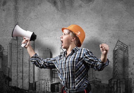 Engineer woman screaming in megaphone and sketches of construction project on wallの写真素材