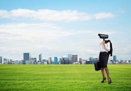 Elegant businesswoman outdoors with suitcase in hand and camera instead of headの写真素材