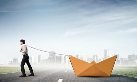 Successful businessman pulling with rope paper boatの写真素材