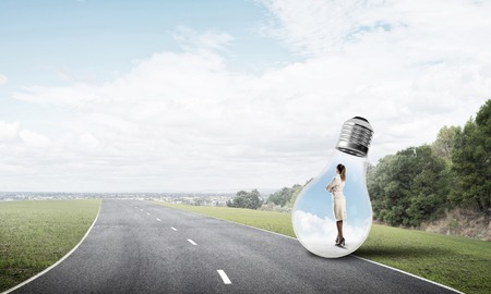 Young businesswoman trapped inside of light bulb on asphalt roadの写真素材