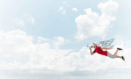 Young cheerful man with megaphone flying high in skyの写真素材