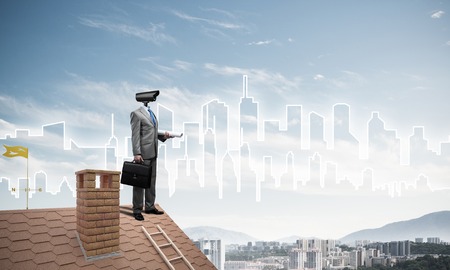 Faceless businessman with camera zoom instead of head standing on house roofの写真素材