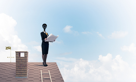 Faceless businesswoman with camera zoom instead of head standing on house roofの写真素材