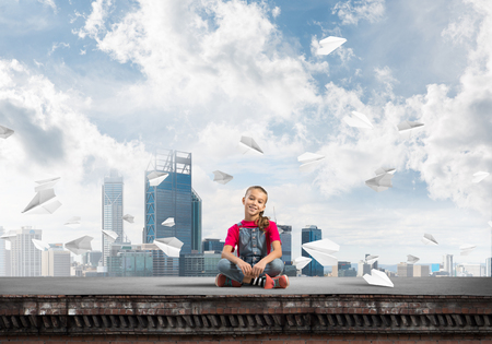 Cute kid girl sitting on building roof and looking in cameraの写真素材