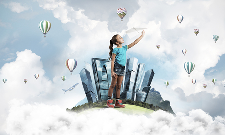 Cute kid girl on city floating island throwing paper planeの写真素材