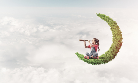 Cute kid girl on green moon in day sky looking in spyglassの写真素材