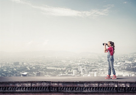 Cute girl of school age on building roof looking in binocularsの写真素材